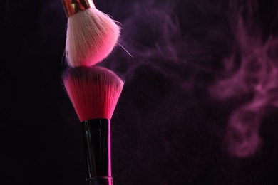 Photo of Makeup brushes with pink eye shadow on black background, closeup. Space for text