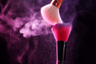 Photo of Makeup brushes with colorful eye shadows in neon lights on black background, closeup. Space for text