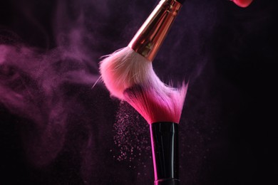 Photo of Makeup brushes with colorful eye shadows in neon lights on black background, closeup