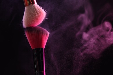 Photo of Makeup brushes with pink eye shadow on black background, closeup. Space for text