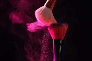 Photo of Makeup brushes with pink eye shadow in neon lights on black background, closeup