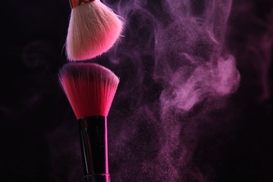 Photo of Makeup brushes with pink eye shadow on black background, closeup. Space for text