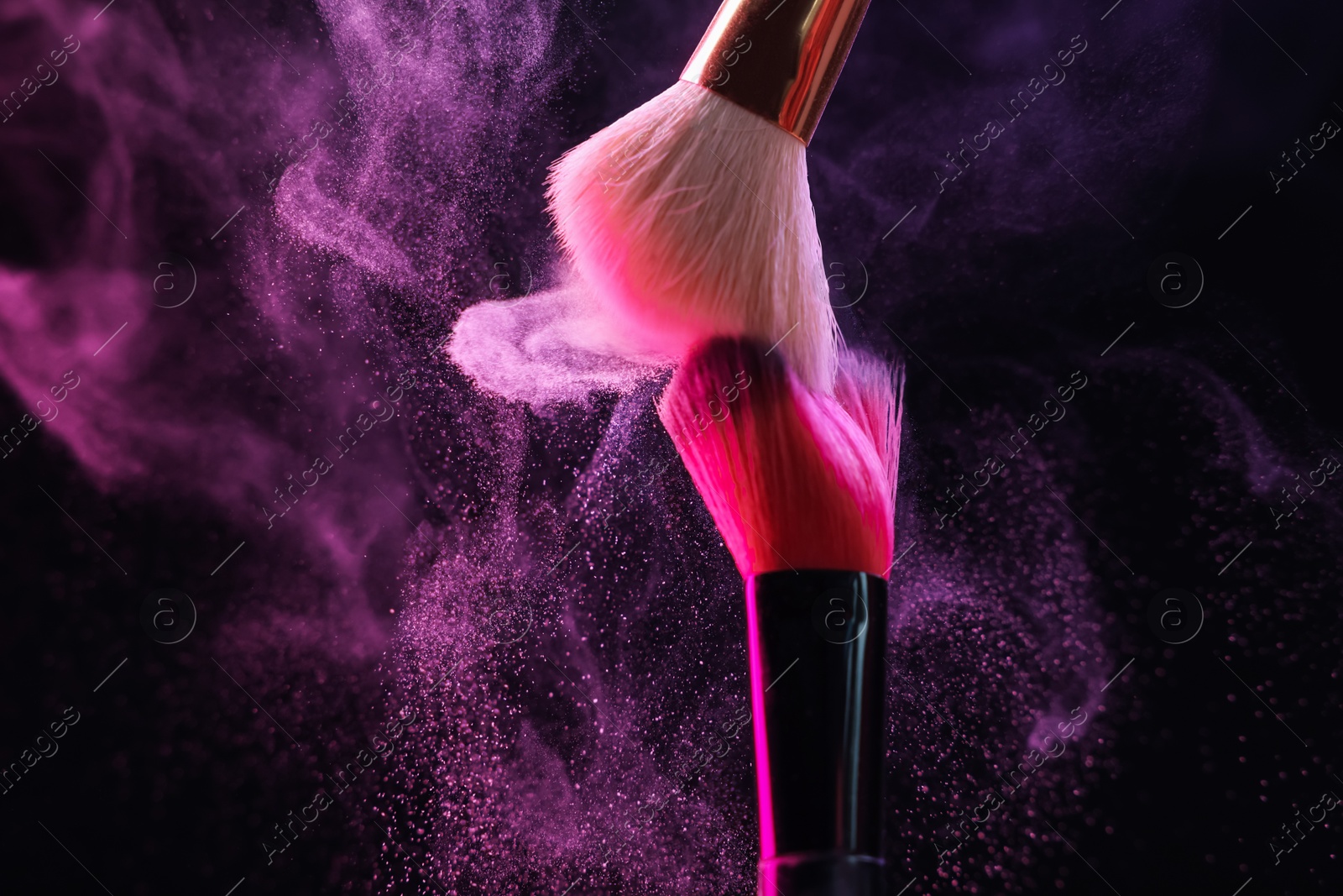 Photo of Makeup brushes with colorful eye shadows in neon lights on black background, closeup