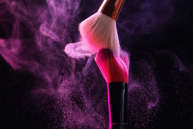 Photo of Makeup brushes with colorful eye shadows in neon lights on black background, closeup