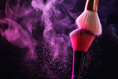 Photo of Makeup brushes with colorful eye shadows in neon lights on black background, closeup. Space for text
