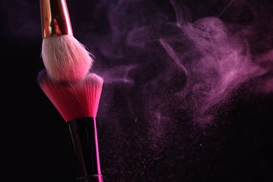 Photo of Makeup brushes with colorful eye shadows in neon lights on black background, closeup. Space for text