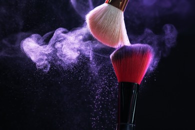 Photo of Makeup brushes with purple eye shadow on black background, closeup. Space for text