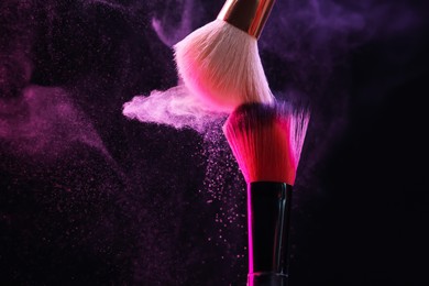 Photo of Makeup brushes with colorful eye shadows in neon lights on black background, closeup