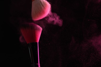 Photo of Makeup brushes with pink eye shadow on black background, closeup. Space for text