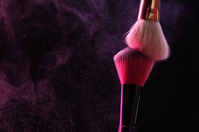 Photo of Makeup brushes with pink eye shadow on black background, closeup. Space for text