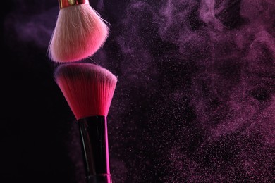 Photo of Makeup brushes with pink eye shadow on black background, closeup. Space for text