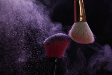 Photo of Makeup brushes with purple eye shadow on black background, closeup