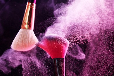 Photo of Makeup brushes with colorful eye shadows in neon lights on black background, closeup