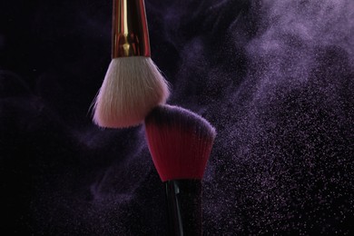 Photo of Makeup brushes with purple eye shadow on black background, closeup