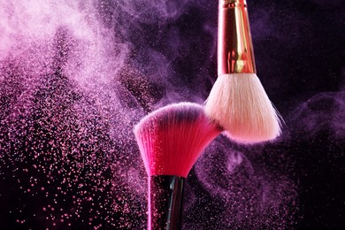 Photo of Makeup brushes with colorful eye shadows in neon lights on black background, closeup
