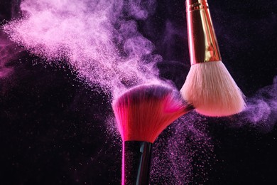 Photo of Makeup brushes with colorful eye shadows in neon lights on black background, closeup