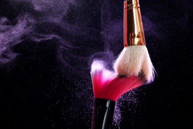 Photo of Makeup brushes with purple eye shadow on black background, closeup. Space for text