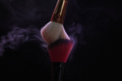 Photo of Makeup brushes with purple eye shadow on black background, closeup