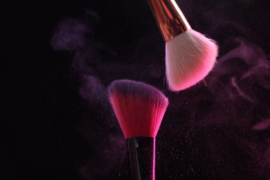 Photo of Makeup brushes with pink eye shadow on black background, closeup