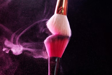 Photo of Makeup brushes with pink eye shadow on black background, closeup