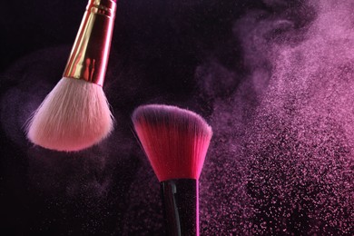Photo of Makeup brushes with pink eye shadow on black background, closeup