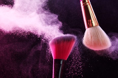 Photo of Makeup brushes with pink eye shadow on black background, closeup