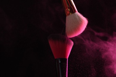 Photo of Makeup brushes with pink eye shadow on black background, closeup