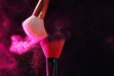 Photo of Makeup brushes with pink eye shadow on black background, closeup