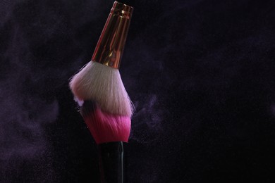 Photo of Makeup brushes with purple eye shadow on black background, closeup
