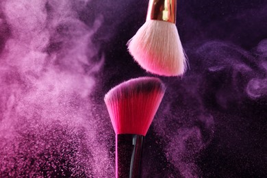 Photo of Makeup brushes with colorful eye shadows in neon lights on black background, closeup