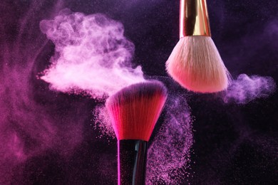 Photo of Makeup brushes with colorful eye shadows in neon lights on black background, closeup