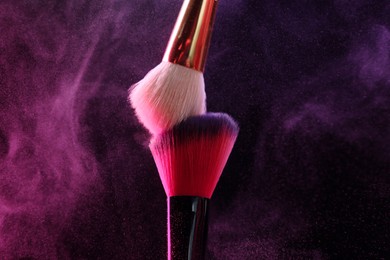 Photo of Makeup brushes with colorful eye shadows in neon lights on black background, closeup