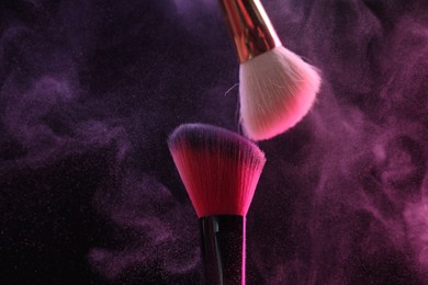 Photo of Makeup brushes with colorful eye shadows in neon lights on black background, closeup