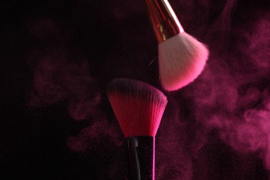 Photo of Makeup brushes with pink eye shadow on black background, closeup