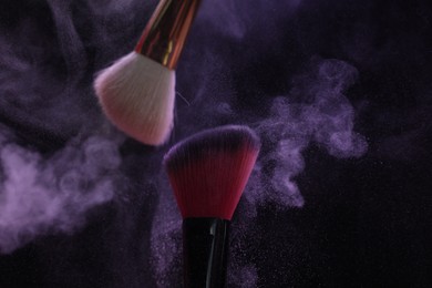 Photo of Makeup brushes with purple eye shadow on black background, closeup