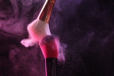 Photo of Makeup brushes with colorful eye shadows in neon lights on black background, closeup