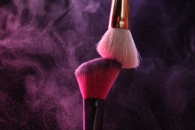 Photo of Makeup brushes with colorful eye shadows in neon lights on black background, closeup