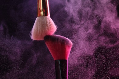 Photo of Makeup brushes with colorful eye shadows in neon lights on black background, closeup