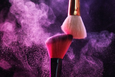 Photo of Makeup brushes with colorful eye shadows in neon lights on black background, closeup