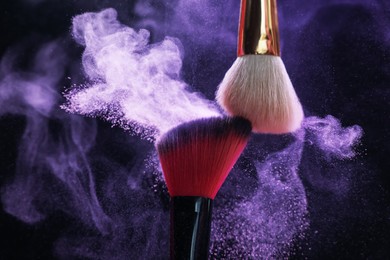Photo of Makeup brushes with purple eye shadow on black background, closeup