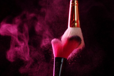 Photo of Makeup brushes with pink eye shadow on black background, closeup