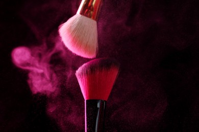 Photo of Makeup brushes with pink eye shadow on black background, closeup