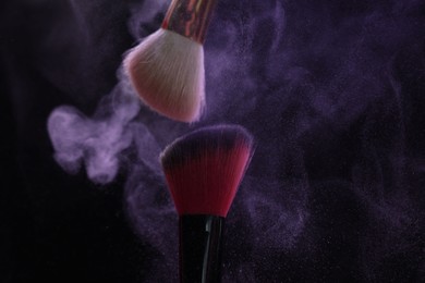 Photo of Makeup brushes with purple eye shadow on black background, closeup
