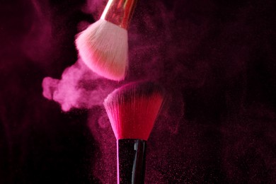 Photo of Makeup brushes with pink eye shadow on black background, closeup