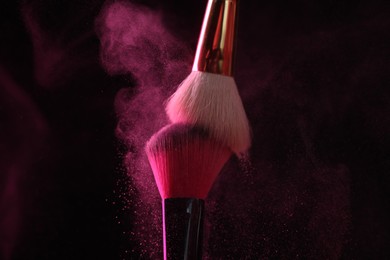 Photo of Makeup brushes with pink eye shadow on black background, closeup