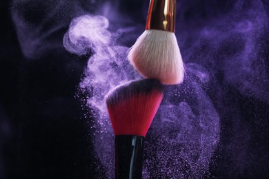 Photo of Makeup brushes with purple eye shadow on black background, closeup