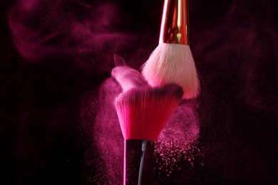 Photo of Makeup brushes with pink eye shadow on black background, closeup