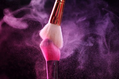 Photo of Makeup brushes with colorful eye shadows in neon lights on black background, closeup