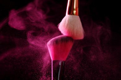 Photo of Makeup brushes with pink eye shadow on black background, closeup