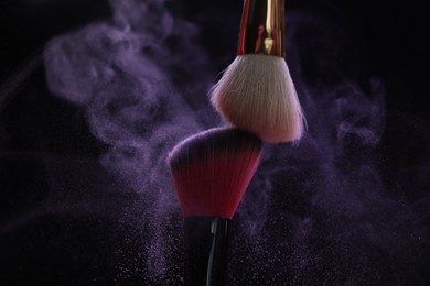 Photo of Makeup brushes with purple eye shadow on black background, closeup